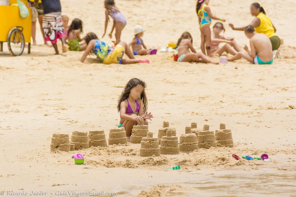 Imagem de uma menina fazendo vários castelinhos de areia na Praia de Curuípe.